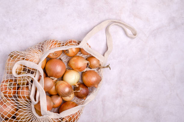 fresh yellow onions in a knitted bag - onion bag netting vegetable imagens e fotografias de stock