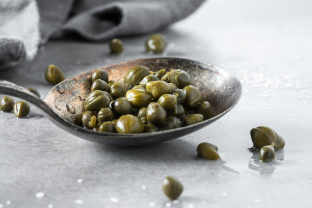 Capers on a Vintage Spoon Capers on a Vintage Spoon caper stock pictures, royalty-free photos & images