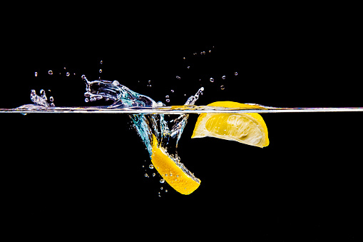 A studio shot of two lemon wedges splashing into water.