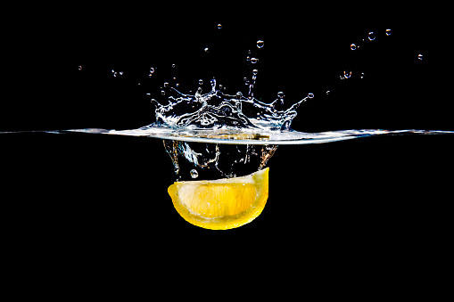 A studio shot of a lemon wedge splashing into water.