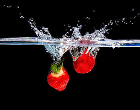 A studio shot of two strawberries splashing into water.
