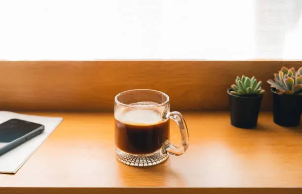 Coffee in a mug on a wooden table with notebooks and small plants.