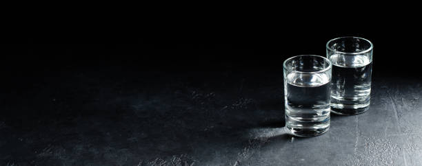 bicchieri di vodka sono di fila su sfondo scuro. messa a fuoco selettiva. spazio di copia - still shot foto e immagini stock