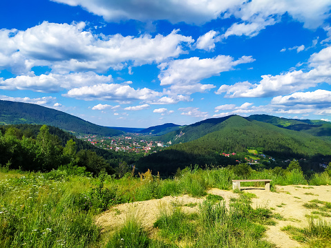 Carpathian landscape with cloudy sky. A wooden bench on a green meadow in mountains near forest. Lifestyle in the Carpathian region. Ecology protection concept. Explore the beauty of the world.