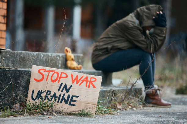 Stop war in Ukraine! Paper placard with 'stop war in Ukraine' message with woman in despair in the background on abandoned city street. peace demonstration photos stock pictures, royalty-free photos & images