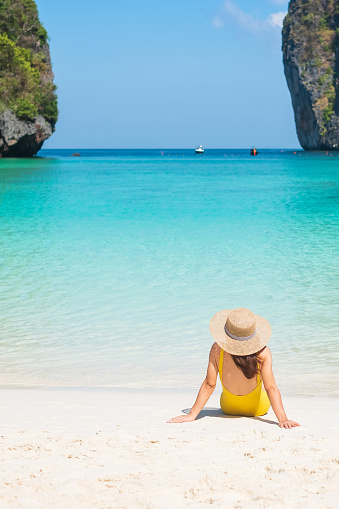 Woman tourist in yellow swimsuit and hat, happy traveller sunbathing at Maya Bay beach on Phi Phi island, Krabi, Thailand. landmark, destination Southeast Asia Travel, vacation and holiday concept