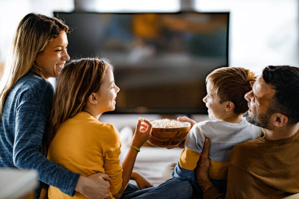 istock Happy family eating popcorn while watching TV at home. 1383755025