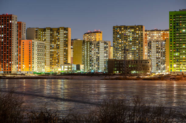 new residential complex under construction on Bank of the sea river in light of night lights reflected in ice stock photo