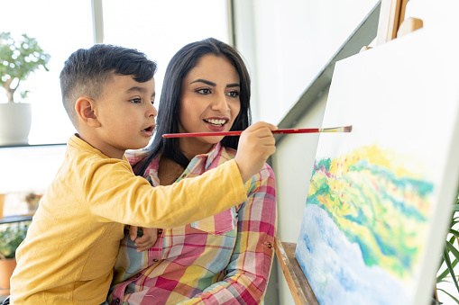 Hispanic mother with son painting a picture at home