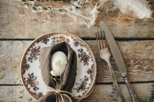 istock Rustic Easter table setting top view. Natural egg in napkin with flowers, setting  with vintage plate, cutlery, pussy willow branches on aged wooden table. Easter table decoration 1383795038