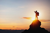 silhouette eines mannes der ein fernglas auf dem berggipfel vor hellem sonnenlicht h%C3%A4lt