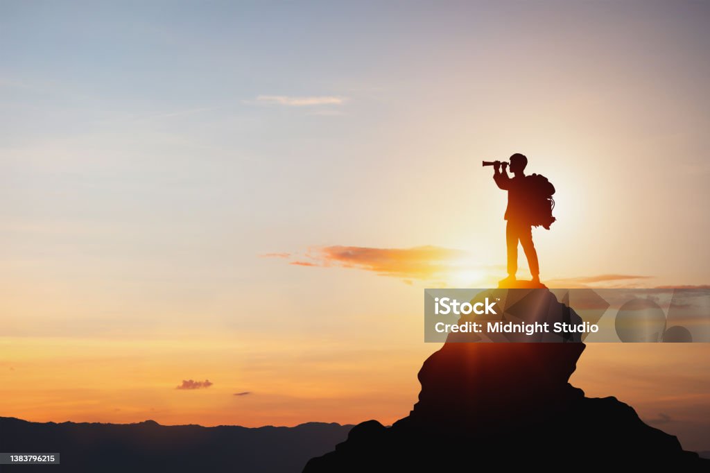 Silhouette of man holding binoculars on mountain peak against bright sunlight sky background. vision for success ideas. businessman's perspective for future planning. Silhouette of man holding binoculars on mountain peak against bright sunlight sky background. The Way Forward Stock Photo