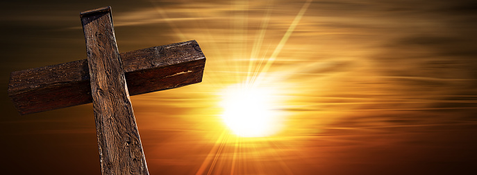 Closeup of a wooden Christian cross against a beautiful sunset with sun rays and copy space. Verona province, Veneto, Italy, Europe.