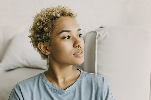 Portrait of mixed race curly-headed girl with natural beauty without make-up wearing nose ring having ideal dark smooth skin looking into the distance with dreamy eyes, thinking of her best future