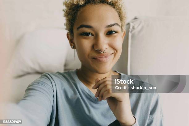 Closeup Of Cute African Ethnicity Girl Recording Stories For Her Blog Using Selfie Camera Of Her Smartphone Sharing Information Dressed In Grey Blue Shirt Posing Against Cosy Home Background Stock Photo - Download Image Now