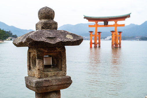 25 march 2019 - Itsukushima, Japan: View of Stone lantern and the Famous Torii gate in high tide of Japanese Inland Sea, on the shore of Miyajima Island.