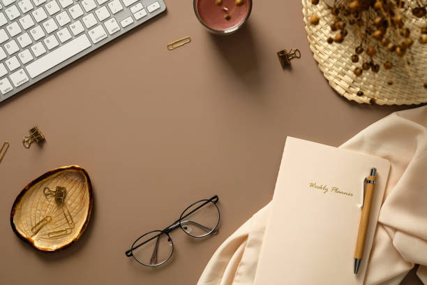 istock Feminine workspace top view. Flat lay keyboard, candle, dried flowers bunch, glasses, weekly planner with pen on brown background. Elegant home office desk table. 1383815258