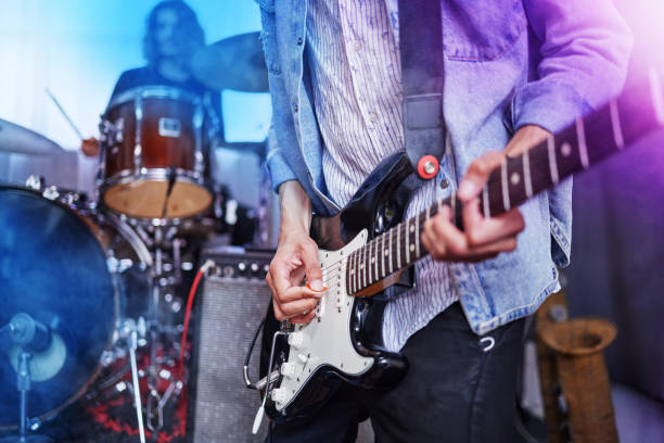 foto recortada de un guitarrista masculino irreconocible actuando en el escenario con sus compañeros de banda de fondo - concierto fotografías e imágenes de stock