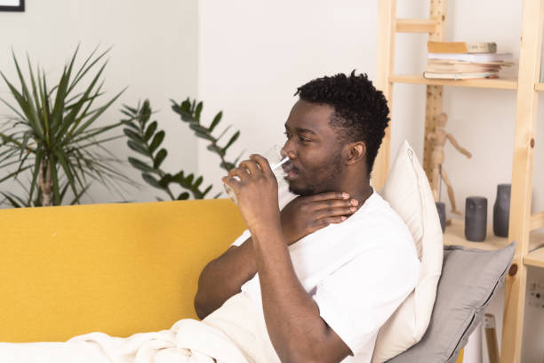 istock Young African man with sore throat waking up and drinking water 1383821671