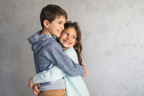 Smiling loving young boy and girl hugging. Portrait of them against grey wall. Copy space.