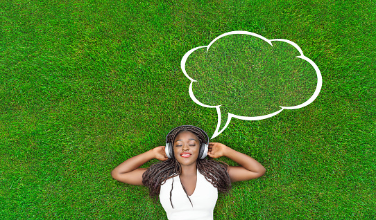 Pretty smiling girl relaxing outdoor. woman listening to music outside with speech bubble and copy space.