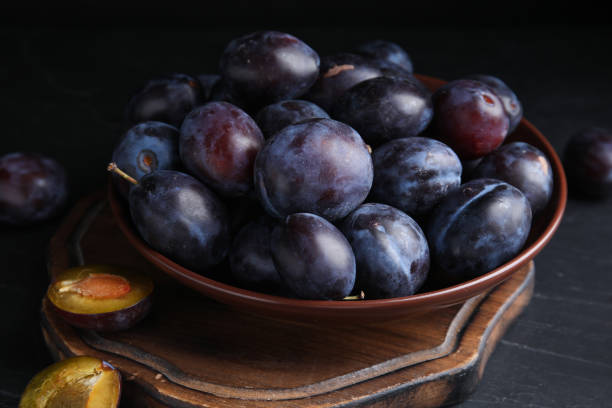 istock Delicious ripe plums in bowl on black table 1383826701
