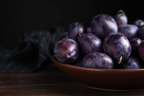 istock Delicious ripe plums in bowl on wooden table, space for text 1383826725