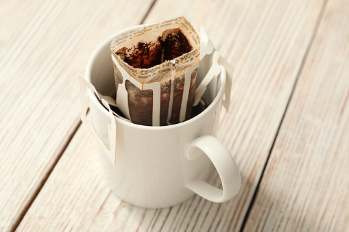 Cup with drip coffee bag on white wooden table, closeup