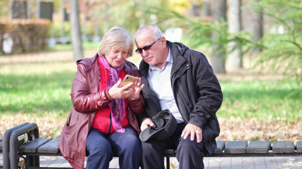 istock Happy senior couple laughing and exciting with something in smartphone mobile while sitting in the park 1383834879
