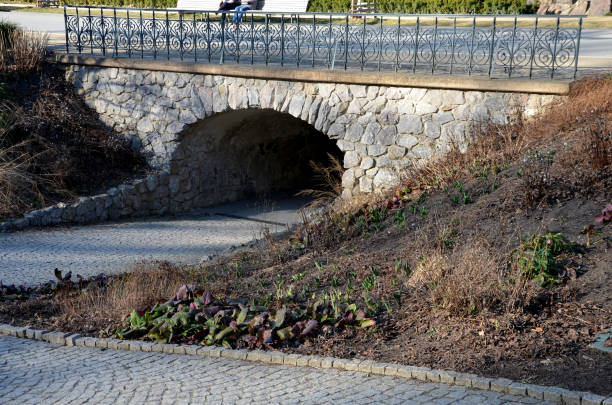 セメントでつながった粗い玄武岩で作られた擁壁。歩行者道路の下のトンネル。地下道は城の庭の歴史的なロマンチックな要素です。花崗岩舗装 - retaining wall flower bed ornamental garden landscaped ストックフォトと画像