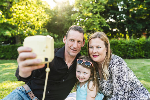 glückliche familie im park mit einem selfie zusammen mit einer instant-print-kamera - instant print transfer stock-fotos und bilder