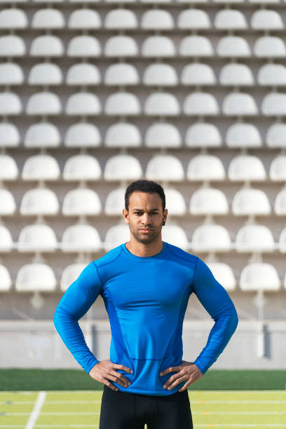 Stock photo of african american athlete in akimbo arms looking at camera in running track.