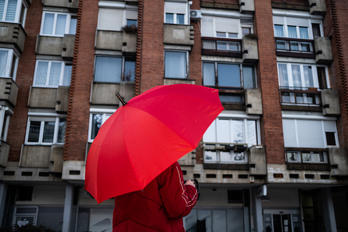 person with a red umbrella in a red jacket, in front of old-fashioned buildings