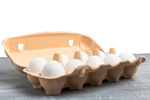 White chicken eggs in carton box on grey textured background.