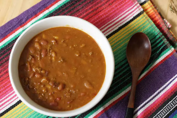 Bowl of Chili With Pinto Beans on Table With Peppers, Spices and Dry Beans in Background