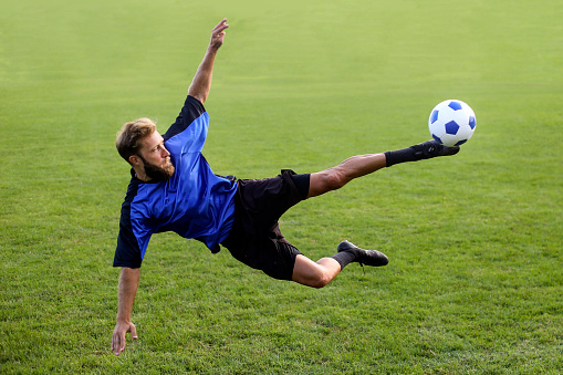 Portrait of young Caucasian soccer football player looks confident practicing kicking ball in motion against white background on green grass. Concept of game, sport, recreation, active lifestyle.