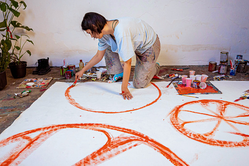 Female painter using a big brush to create a large scale still life painting with oranges only
