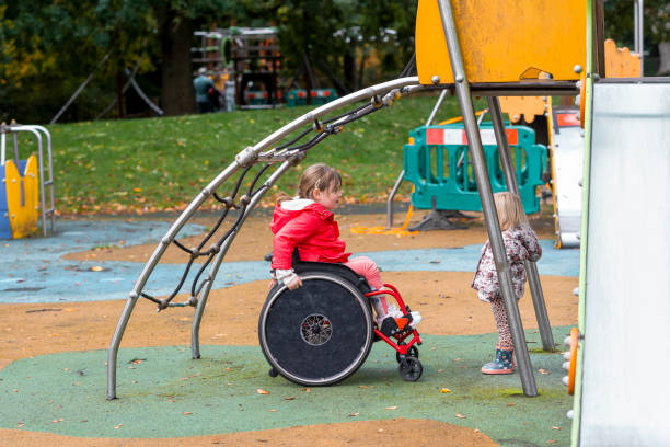 A wide-angle side view of two little girls playing together in a playground of a public park in Newcastle upon Tyne. The youngest is playing underneath the climbing frame.