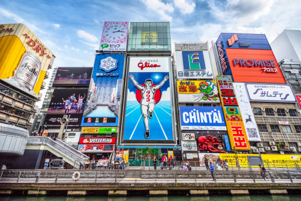 Dotonbori shopping street in Osaka, Japan Tourists and locals walk below the famed advertisements lining Dotonbori Canal at. The district is one of Osaka's primary tourist destinations. osaka city photos stock pictures, royalty-free photos & images
