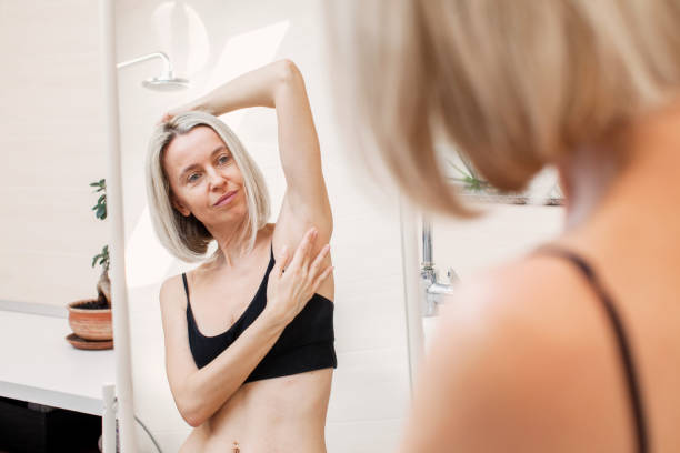 frau mittleren alters, die sich bei der selbstuntersuchung der brust in einen spiegel schaut - breast breast cancer breast examination cancer stock-fotos und bilder