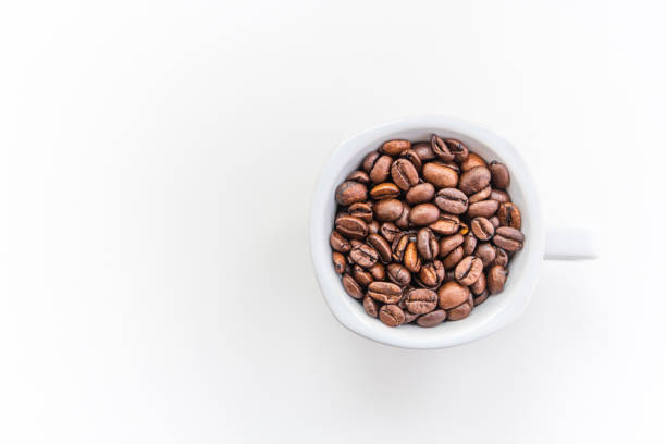 A white coffee cup filled with coffee beans on a white minimalist background