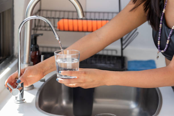 frauenhände, die ein glas halten, das sich mit wasser aus dem wasserhahnfilter füllt - destilliertes wasser stock-fotos und bilder