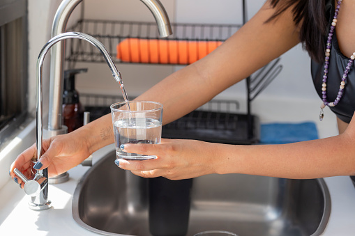 Woman's hands holding a glass that fills with water from the tap filter.