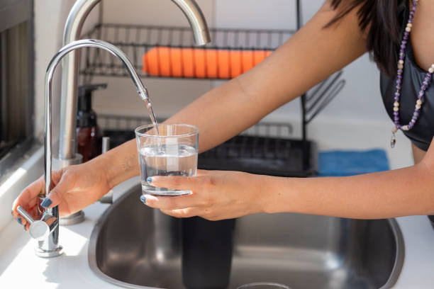 Woman's hands holding a glass that fills with water from the tap filter Woman's hands holding a glass that fills with water from the tap filter. purified water stock pictures, royalty-free photos & images