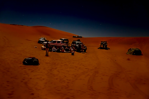Djanet, Algeria -December 19, 2021: 4X4 vehicles parked, red colored sand dunes, stars in dark sky. Long exposure photograph