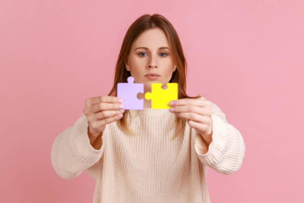 concentrated attractive blond woman holding yellow and purple puzzle pieces, solving tasks. - jigsaw puzzle solution one person people imagens e fotografias de stock