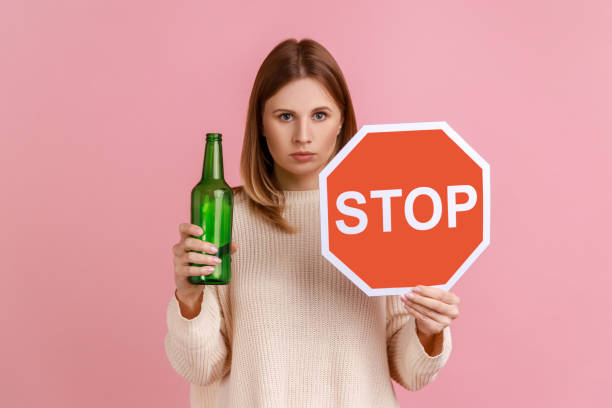 femme sérieuse tenant un panneau d’arrêt rouge et une bouteille avec une boisson alcoolisée, appelle à ne pas boire d’alcool. - eastern european caucasian one person alcoholism photos et images de collection