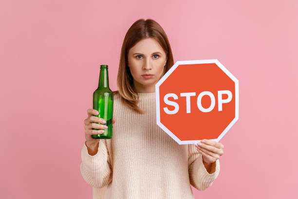 Serious woman holding red stop sign and bottle with alcoholic beverage, calls on dont drink alcohol. stock photo