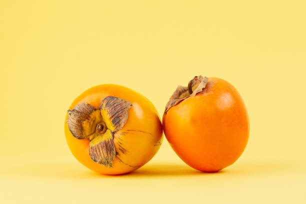 istock Two persimmons closeup on yellow background 1383882009