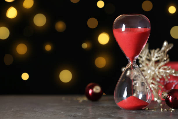 istock Hourglass with flowing sand and decor on grey table against blurred lights, space for text. Christmas countdown 1383882049